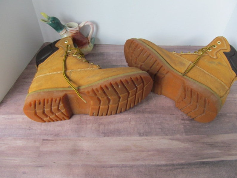 Op de afbeelding: Een paar bruine leren werkschoenen met zwarte accenten en een dikke rubberen zool. De schoenen zijn gedragen en hebben een vintage uitstraling.