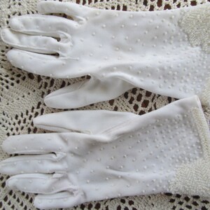 May include: A pair of white cotton gloves with a dotted pattern. The gloves have a beaded trim around the wrist.