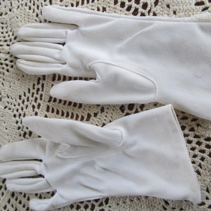 May include: A pair of white cotton gloves. The gloves are made of a soft, smooth fabric and have a simple, classic design.