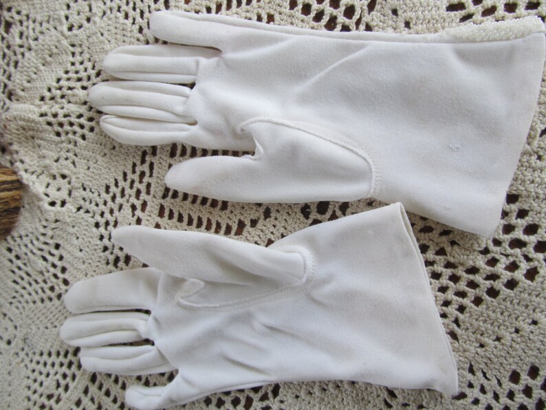 May include: A pair of white cotton gloves. The gloves are made of a soft, smooth fabric and have a simple, classic design.