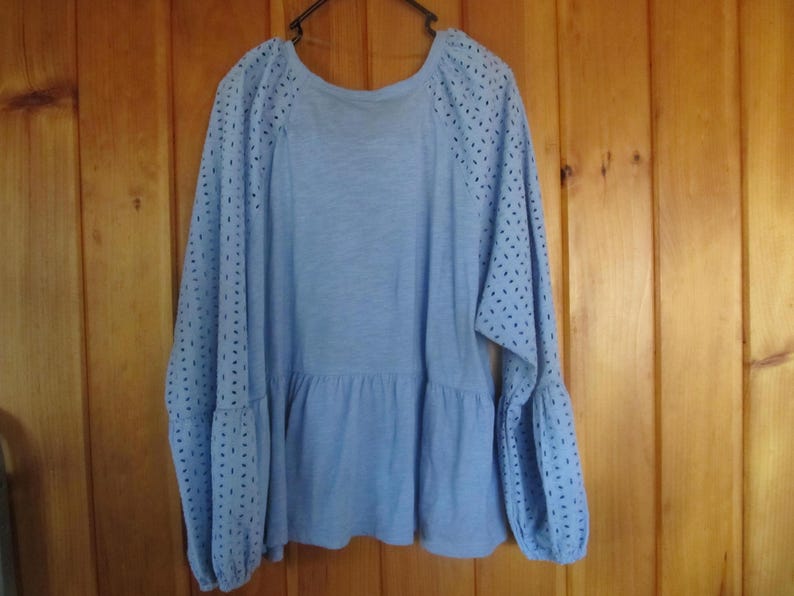 Pu&ograve; includere: Una blusa azzurra a maniche lunghe con vita arricciata e dettagli a occhiello sulle maniche.