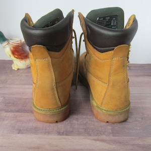 Op de afbeelding: Een paar bruine leren werkschoenen met bruine leren afwerking rond de bovenkant. De schoenen hebben veters en een dikke zool.