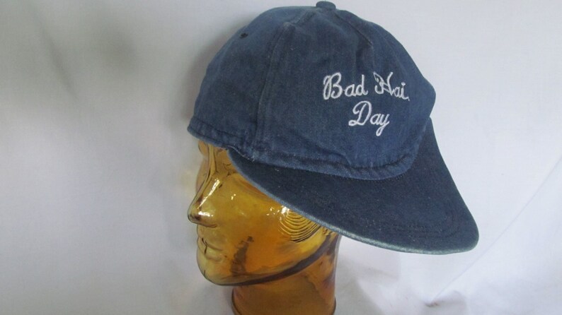 May include: A blue denim baseball cap with a white embroidered message that reads "Bad Hair Day".