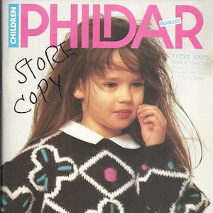May include: A young girl wearing a black and white sweater with colorful geometric patterns. The sweater has a white collar and is knit with a fuzzy yarn. The girl has long brown hair and is looking at the camera. The text on the magazine cover reads "PHILDAR" and "ZORRO IS BACK... AND BLACK IS IN. GET BACK TO SCHOOL WITH STYLE!"