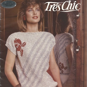 May include: A knitting pattern booklet titled Patons Tres Chic featuring a short-sleeved, boat-neck top in a light, textured knit. The top displays a diagonal pattern with a prominent rust-colored floral motif on the front and a matching design.