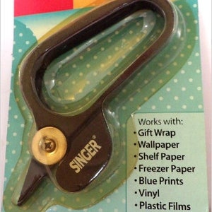 May include: A black and silver rolling edge cutter with the brand name "SINGER" printed on the side. The cutter is designed for cutting gift wrap, wallpaper, shelf paper, freezer paper, blue prints, vinyl, plastic films, and more.