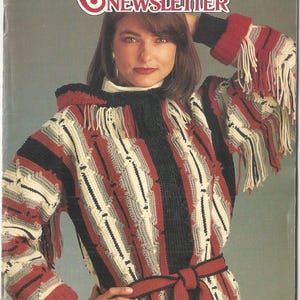 May include: Cover of "Annie's Crochet Newsletter" magazine. The cover features a woman wearing a long, hooded crochet coat with red, black, white, and gray stripes. The coat has fringe on the sleeves and a red belt. The magazine title is in red.