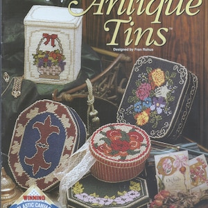 May include: A collection of five plastic canvas needlepoint projects featuring antique tin designs. The designs include a basket of flowers, a floral bouquet, a fleur-de-lis, a rose bouquet, and orchids. The title of the project is "Antique Tins" and the designer is Fran Rohus.