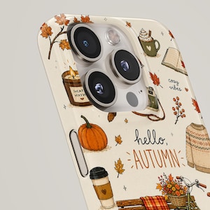 May include: A cream-colored phone case featuring a repeating autumn-themed pattern including a pumpkin, a sweater, a bicycle with a flower basket, a candle, a coffee cup, and falling leaves. The text "hello, AUTUMN" and "cozy vibes" is printed.