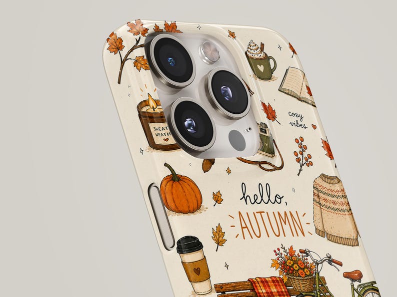May include: A cream-colored phone case featuring a repeating autumn-themed pattern including a pumpkin, a sweater, a bicycle with a flower basket, a candle, a coffee cup, and falling leaves. The text "hello, AUTUMN" and "cozy vibes" is printed.