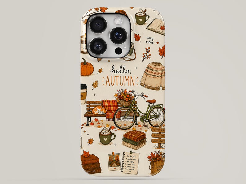 May include: A cream-colored phone case featuring an autumn-themed pattern with pumpkins, a bicycle, a sweater, mugs of hot cocoa, stacks of books, and fallen leaves. The text hello, AUTUMN is printed in the center with additional cozy vibes text.