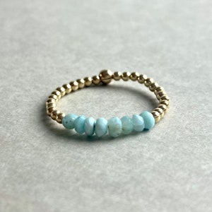 Puede incluir: Un brazalete de cuentas doradas con una fila de cuentas de piedras preciosas de color azul claro.