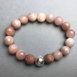 Könnte beinhalten: Ein Armband aus rosafarbenen und weißen Sunstone-Perlen mit einem silbernen und braunen Perlenanhänger.