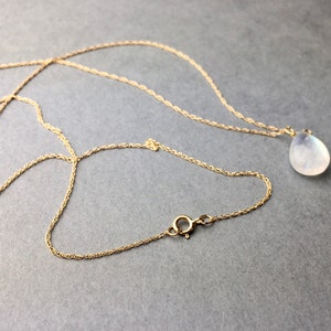May include: A gold chain necklace with a teardrop-shaped moonstone pendant.
