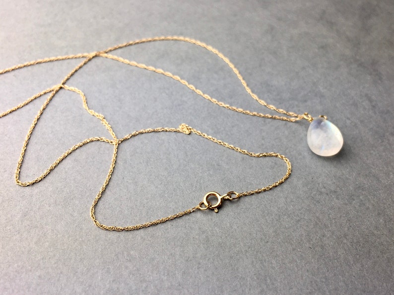 May include: A gold chain necklace with a teardrop-shaped moonstone pendant.