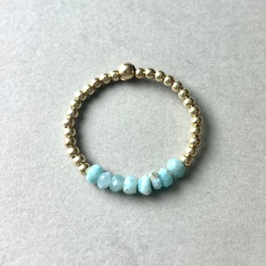 Puede incluir: Un brazalete de cuentas doradas con una fila de cuentas de piedras preciosas de color azul claro.