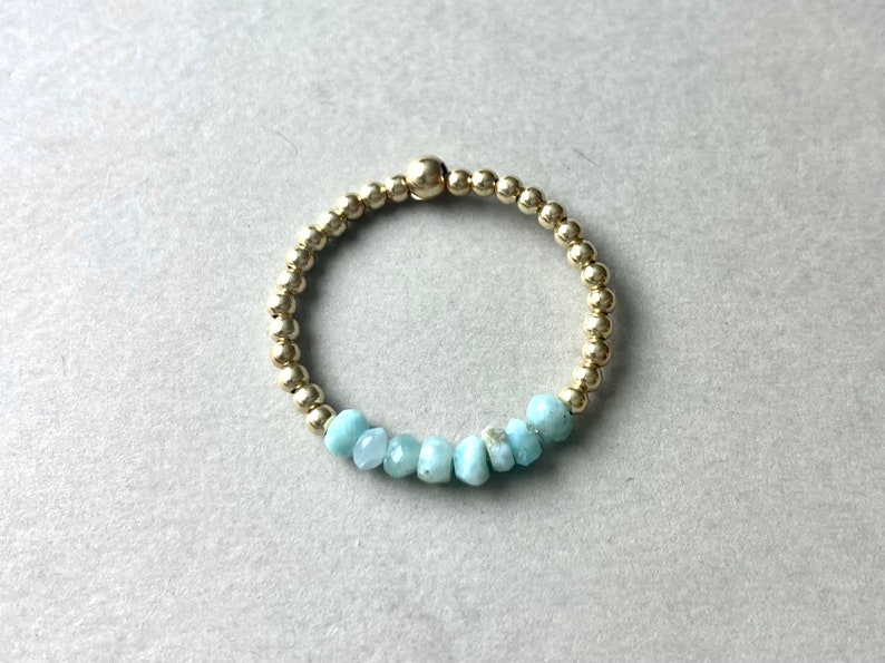 Puede incluir: Un brazalete de cuentas doradas con una fila de cuentas de piedras preciosas de color azul claro.