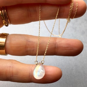 May include: A delicate gold chain necklace with a teardrop-shaped moonstone pendant.