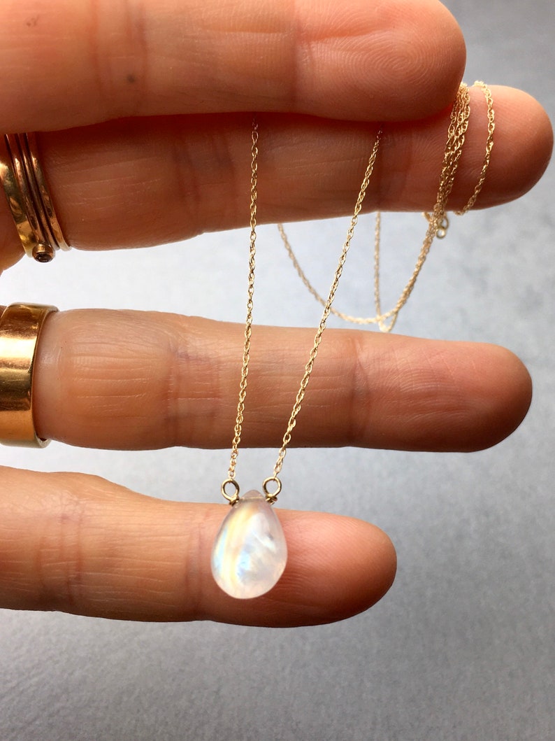 May include: A delicate gold chain necklace with a teardrop-shaped moonstone pendant.