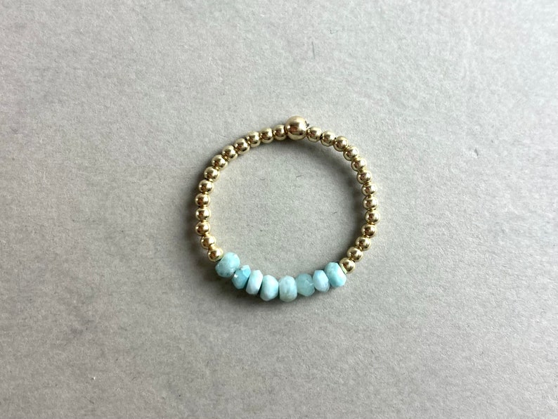 Puede incluir: Un brazalete de cuentas doradas con una fila de cuentas de piedras preciosas de color azul claro.