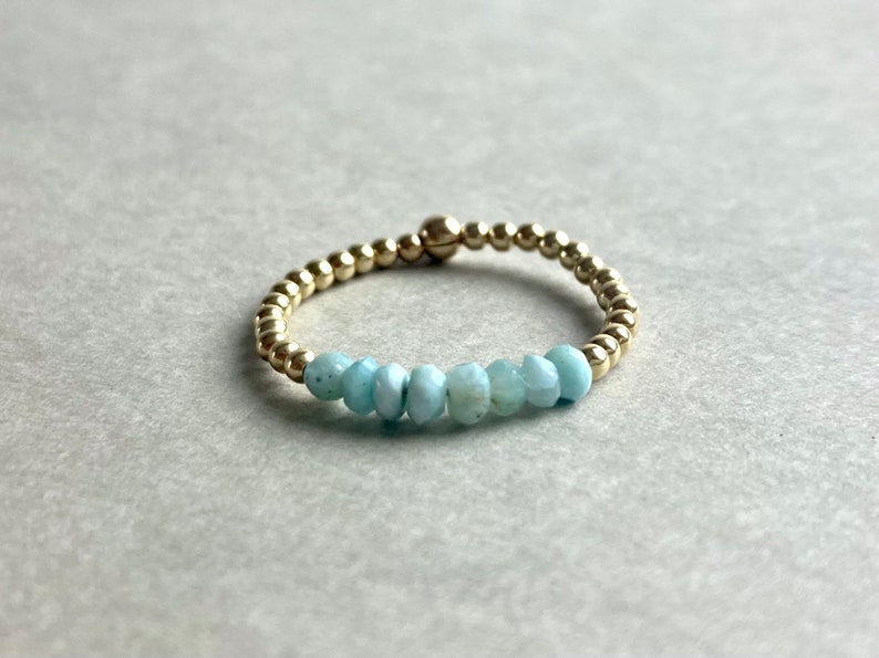 Puede incluir: Un brazalete de cuentas doradas con una fila de cuentas de piedras preciosas de color azul claro.