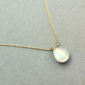 May include: A delicate gold chain necklace with a teardrop-shaped moonstone pendant.