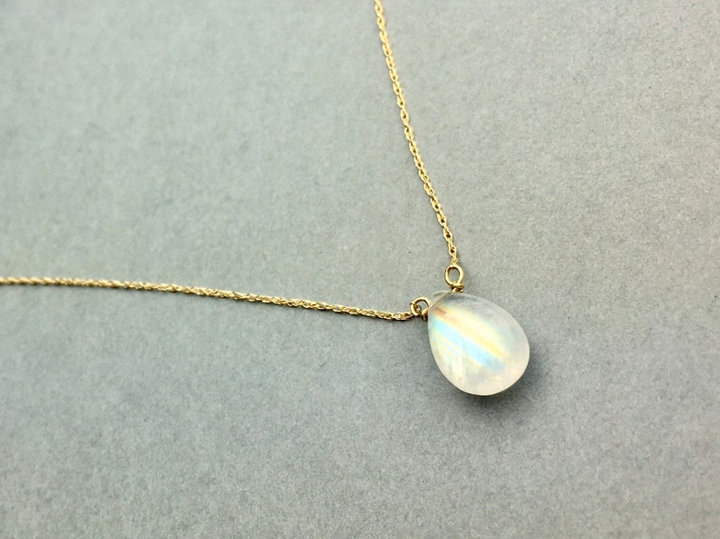 May include: A delicate gold chain necklace with a teardrop-shaped moonstone pendant.