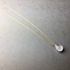 May include: A delicate gold chain necklace with a teardrop-shaped white gemstone pendant.