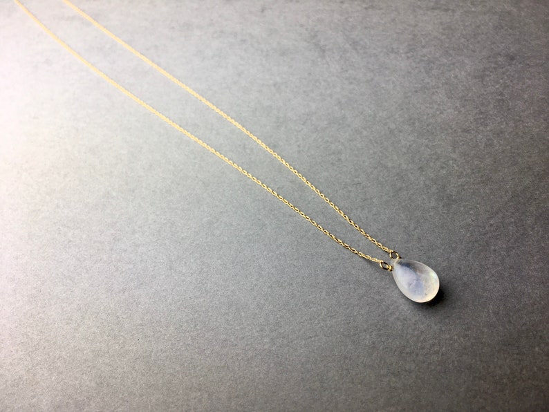 May include: A delicate gold chain necklace with a teardrop-shaped white gemstone pendant.