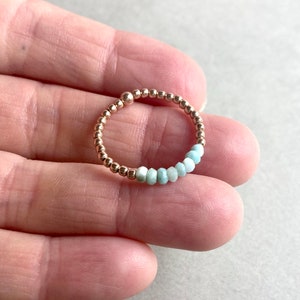 Puede incluir: Un delicado anillo hecho de cuentas doradas con una fila de cuentas de piedras preciosas de color azul claro.