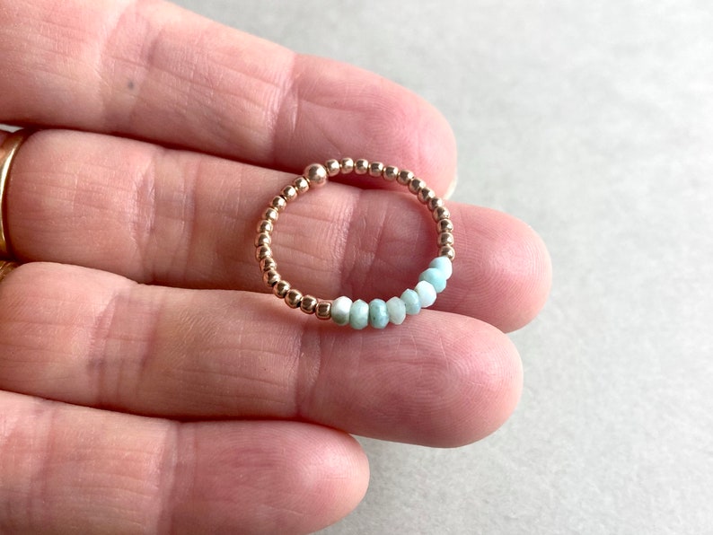 Puede incluir: Un delicado anillo hecho de cuentas doradas con una fila de cuentas de piedras preciosas de color azul claro.
