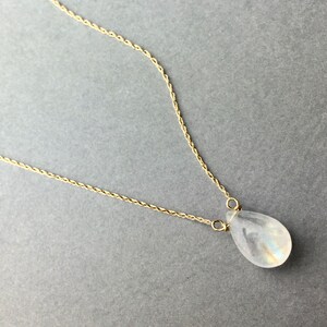 May include: A delicate gold chain necklace with a teardrop-shaped moonstone pendant.