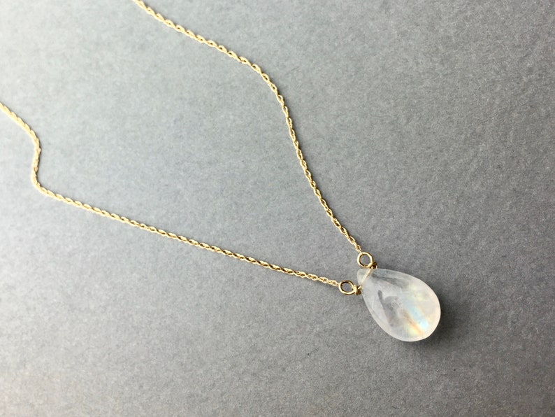 May include: A delicate gold chain necklace with a teardrop-shaped moonstone pendant.