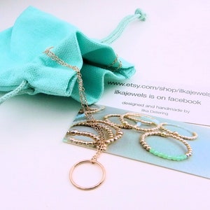 May include: A gold necklace with a circle pendant, packaged in a turquoise drawstring bag. The necklace is displayed on a card with the text "www.etsy.com/shop/ilkajewels ilkajewels is on facebook designed and handmade by Ilka Detering".