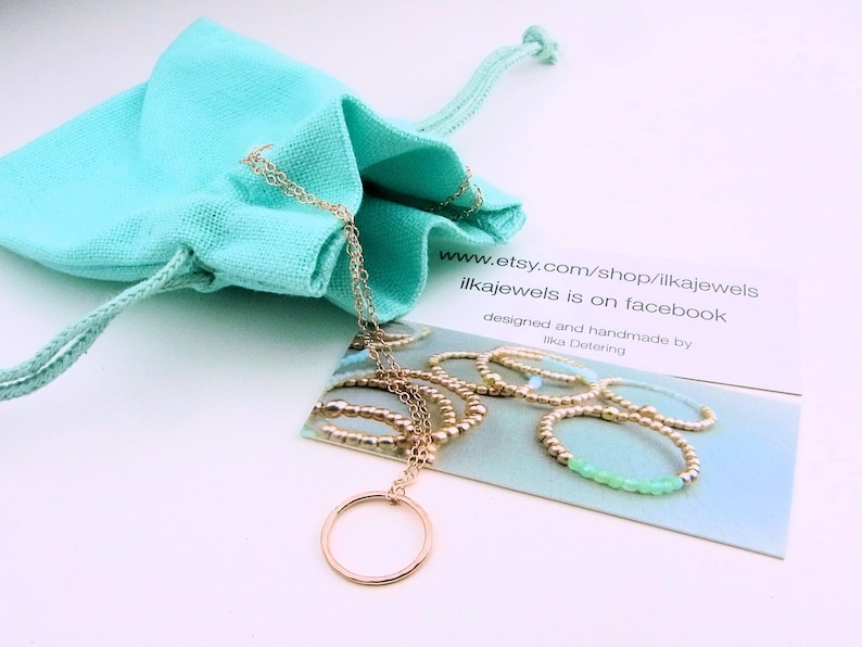 May include: A gold necklace with a circle pendant, packaged in a turquoise drawstring bag. The necklace is displayed on a card with the text "www.etsy.com/shop/ilkajewels ilkajewels is on facebook designed and handmade by Ilka Detering".