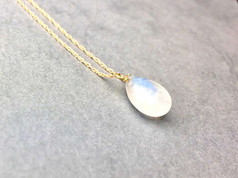 May include: A gold chain necklace with a teardrop-shaped moonstone pendant.