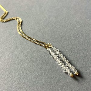 以下が含まれることがあります： 金色のチェーンに、透明なクリスタルビーズが2本糸でぶら下がっている。チェーンは金色のピンに繋がっている。