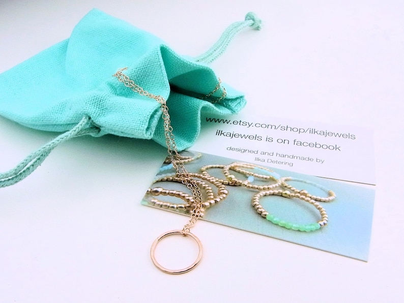 Puede incluir: Un collar de oro con un colgante circular, empaquetado en una bolsa de cord&oacute;n turquesa. El collar se muestra en una tarjeta con el texto "www.etsy.com/shop/ilkajewels ilkajewels is on facebook designed and handmade by Ilka Detering".