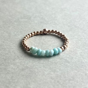 Puede incluir: Un delicado anillo de oro con una fila de cuentas de piedras preciosas de color azul claro.
