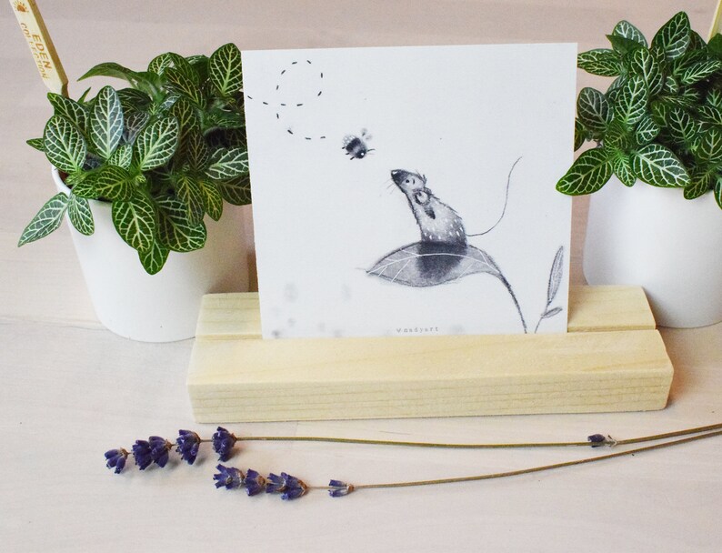 May include: A black and white illustration of a mouse on a leaf with a bee flying nearby. The illustration is printed on a white card and displayed on a wooden stand.