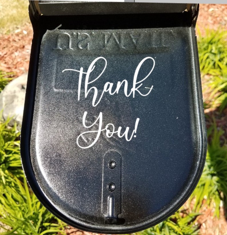 Puede incluir: Una puerta de buz&oacute;n de metal negro con el texto Thank You! en letra cursiva blanca sobre la superficie. La puerta tiene un acabado met&aacute;lico brillante e incluye un mecanismo de cierre vertical central con dos remaches visibles.
