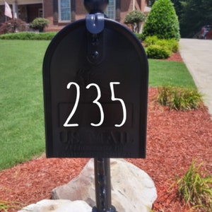 Puede incluir: Un buz&oacute;n de metal negro con el n&uacute;mero de casa 235 en blanco en la puerta frontal. El buz&oacute;n tiene una parte superior redondeada, un remate decorativo y texto en relieve que dice U.S. MAIL APPROVED BY THE POSTMASTER GENERAL.