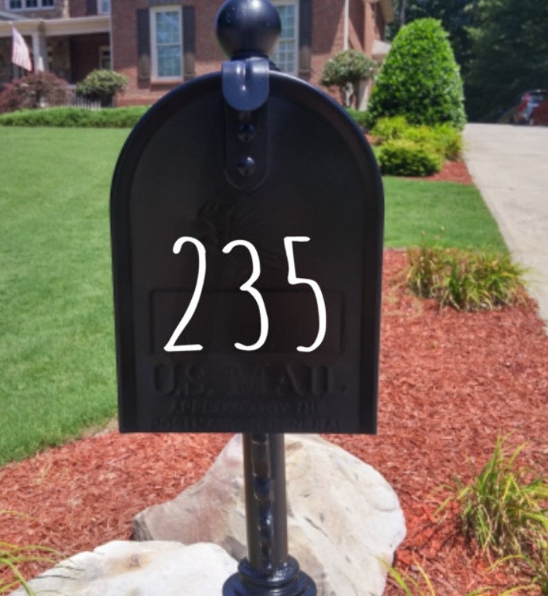 Puede incluir: Un buz&oacute;n de metal negro con el n&uacute;mero de casa 235 en blanco en la puerta frontal. El buz&oacute;n tiene una parte superior redondeada, un remate decorativo y texto en relieve que dice U.S. MAIL APPROVED BY THE POSTMASTER GENERAL.