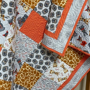 May include: A patchwork quilt with a variety of animal prints, including giraffe, fox, and owl. The quilt is made with a variety of fabrics in shades of gray, brown, orange, and white. The quilt is edged with a bright orange trim.