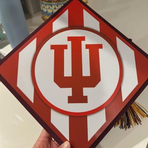 A person is holding a graduation cap with the Indiana University logo on it.
