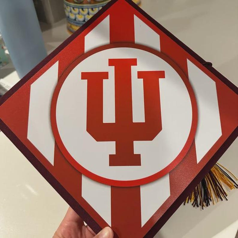 A person is holding a graduation cap with the Indiana University logo on it.