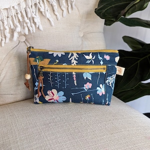 May include: A small blue zippered pouch with a floral print and yellow accents. The pouch has a wooden bead zipper pull and a small fabric tag.