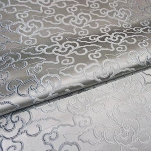 May include: Silver fabric with an embossed cloud pattern. The fabric is folded in half, showing the pattern on both sides.