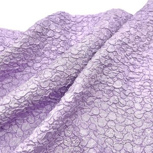 May include: A close-up of a textured, lilac fabric with a raised pattern. The fabric is soft and has a subtle sheen.