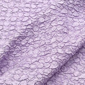 May include: Close-up of a textured fabric with a light purple color. The fabric has a raised, pebble-like pattern.